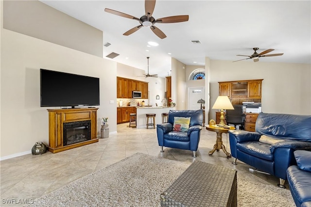 living room featuring visible vents, a ceiling fan, a glass covered fireplace, high vaulted ceiling, and baseboards