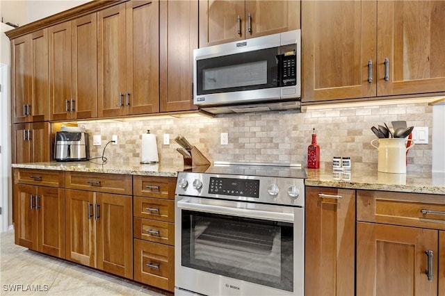 kitchen featuring stainless steel appliances, brown cabinets, backsplash, and light stone countertops