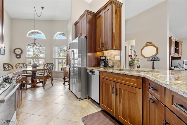 kitchen with light stone counters, a sink, appliances with stainless steel finishes, decorative backsplash, and brown cabinetry