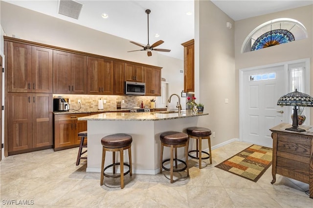 kitchen featuring light stone counters, stainless steel appliances, visible vents, a sink, and a kitchen bar