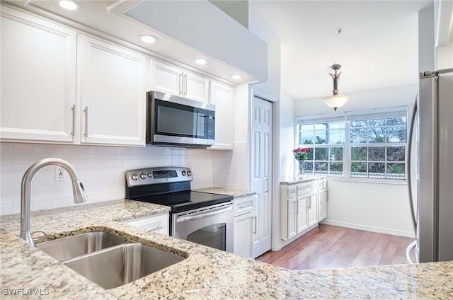 kitchen featuring light stone counters, stainless steel appliances, tasteful backsplash, white cabinets, and a sink