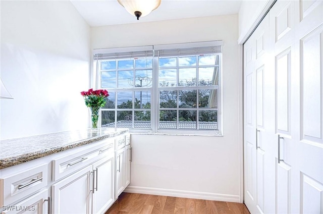 interior space with light stone counters, white cabinets, light wood-style flooring, and baseboards