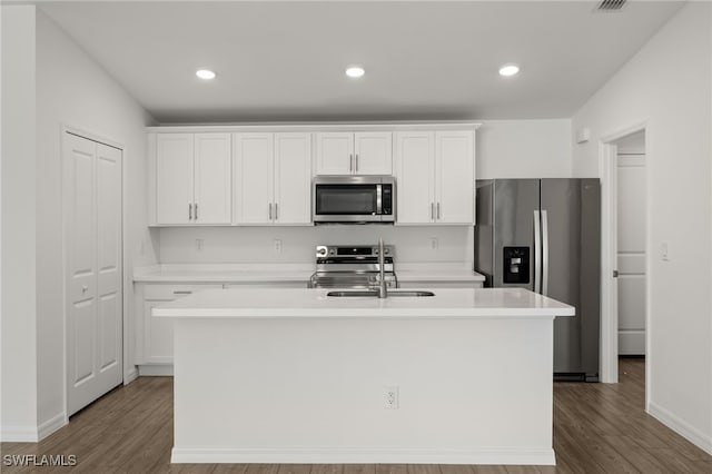 kitchen with stainless steel appliances, wood finished floors, a kitchen island with sink, and white cabinets