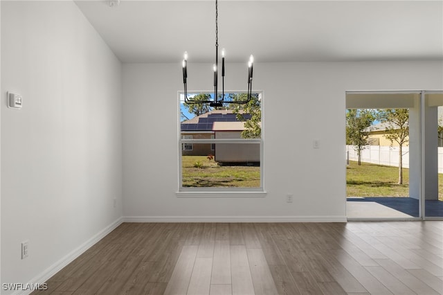 unfurnished dining area featuring a notable chandelier, baseboards, and wood finished floors