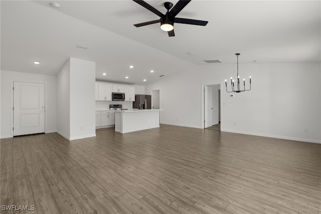 unfurnished living room featuring ceiling fan with notable chandelier, visible vents, baseboards, vaulted ceiling, and light wood-style floors