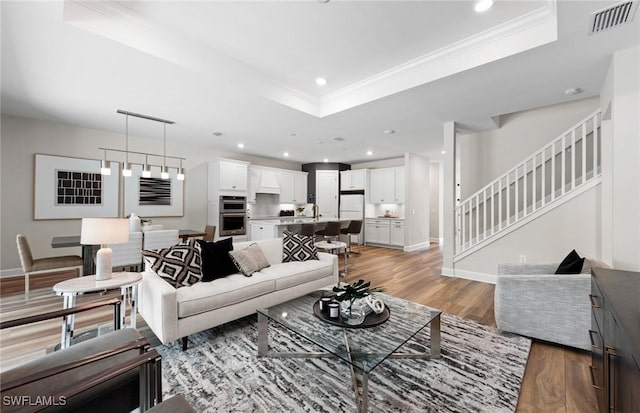 living area with visible vents, a raised ceiling, wood finished floors, crown molding, and recessed lighting