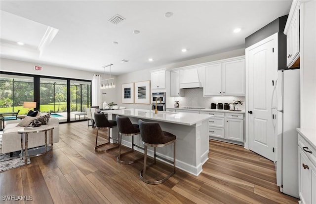 kitchen featuring a kitchen island with sink, light countertops, freestanding refrigerator, and white cabinets