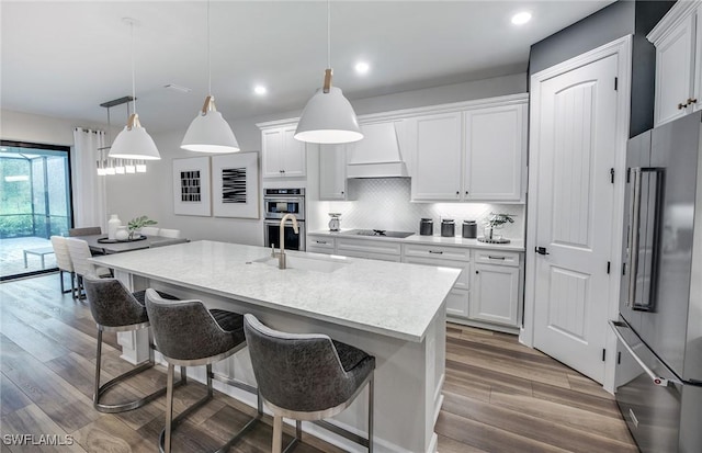 kitchen featuring decorative light fixtures, white cabinetry, light countertops, appliances with stainless steel finishes, and a center island with sink