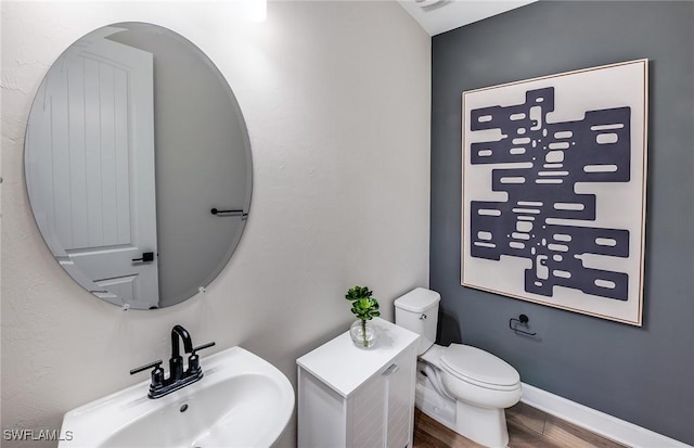 half bathroom with baseboards, a sink, toilet, and wood finished floors