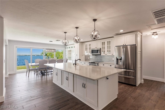 kitchen with a center island with sink, glass insert cabinets, a water view, stainless steel appliances, and light countertops