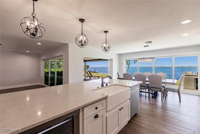 kitchen with dishwasher, decorative light fixtures, a water view, light stone countertops, and a sink