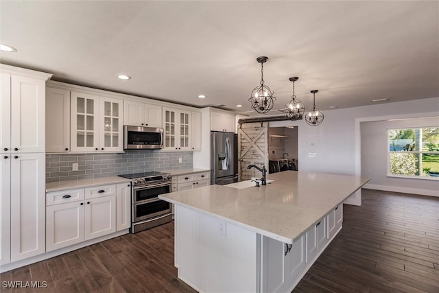 kitchen featuring a center island with sink, appliances with stainless steel finishes, glass insert cabinets, white cabinetry, and a sink