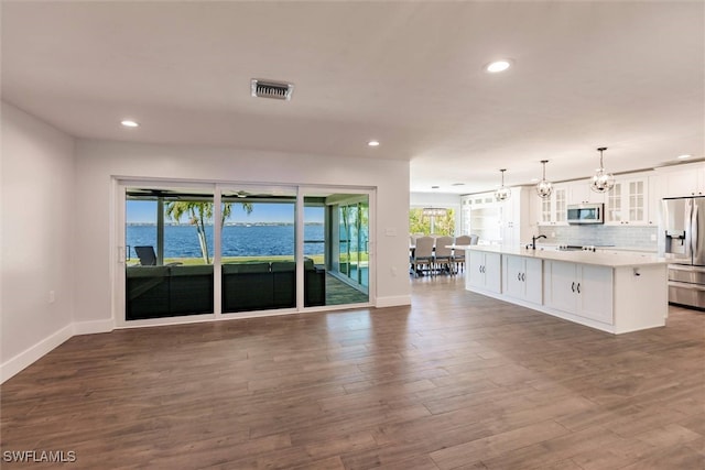 unfurnished living room with baseboards, visible vents, dark wood-style flooring, a water view, and recessed lighting