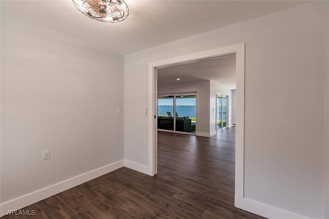 unfurnished room with a water view, dark wood finished floors, and baseboards