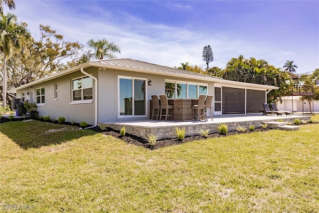 rear view of house featuring a patio, stucco siding, a lawn, a standing seam roof, and metal roof