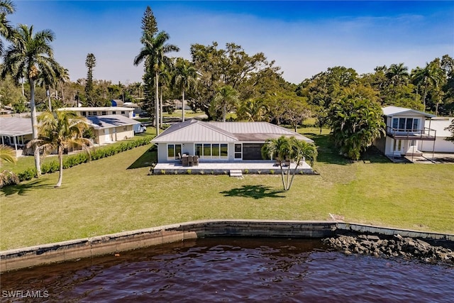 rear view of house featuring a water view, a patio area, and a lawn