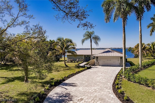 ranch-style home with metal roof, a water view, a standing seam roof, decorative driveway, and a front lawn