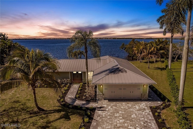 view of front of home with an attached garage, metal roof, decorative driveway, and a water view