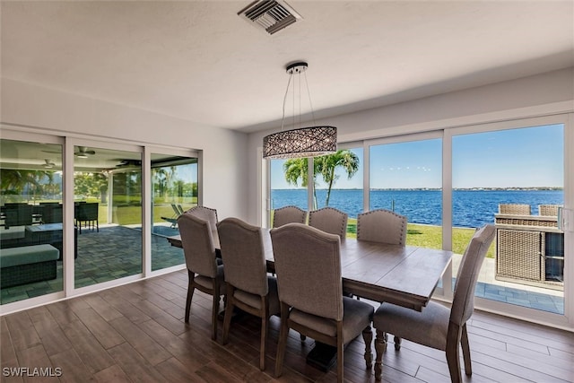 dining space with dark wood-style floors, a water view, visible vents, and a healthy amount of sunlight