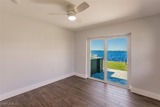 unfurnished room with dark wood-style floors, a water view, a ceiling fan, and baseboards