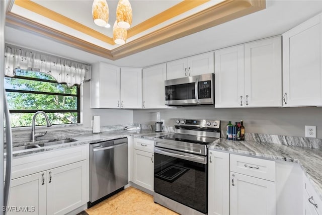 kitchen with appliances with stainless steel finishes, light stone countertops, a tray ceiling, white cabinetry, and a sink