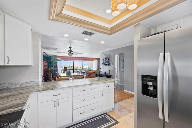 kitchen with a tray ceiling, visible vents, white cabinets, stainless steel fridge, and a peninsula