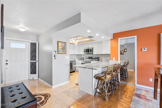 kitchen with a breakfast bar area, a peninsula, baseboards, white cabinets, and appliances with stainless steel finishes