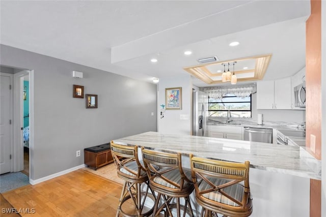 kitchen with white cabinets, appliances with stainless steel finishes, a peninsula, a tray ceiling, and a sink