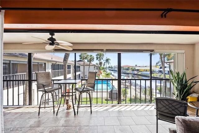 sunroom / solarium with a ceiling fan and a water view