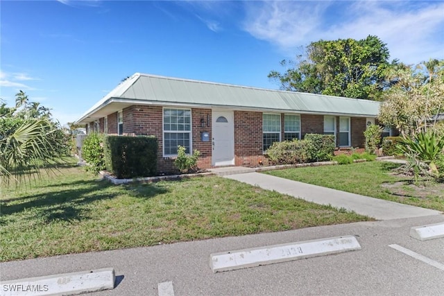 single story home with metal roof, a front lawn, and brick siding