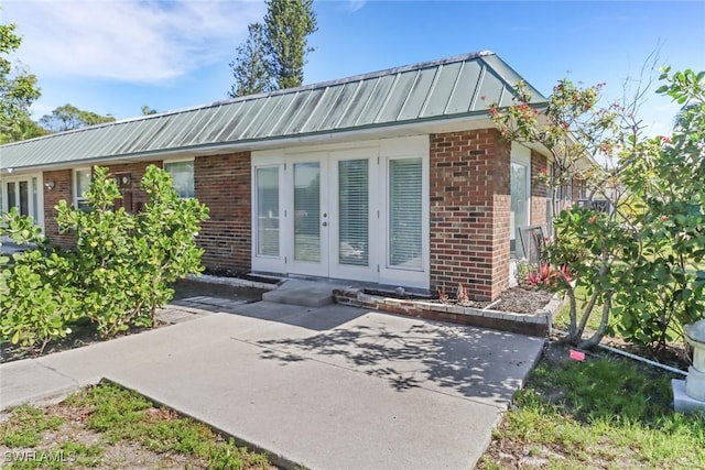 exterior space with a standing seam roof, metal roof, french doors, and brick siding