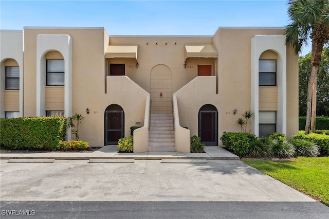 view of front of property featuring uncovered parking, stairway, and stucco siding