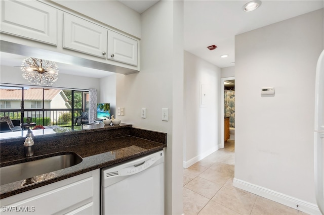 kitchen featuring light tile patterned floors, dark stone counters, dishwasher, white cabinetry, and a sink