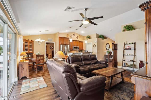 living room with ceiling fan with notable chandelier, lofted ceiling, visible vents, and wood finished floors