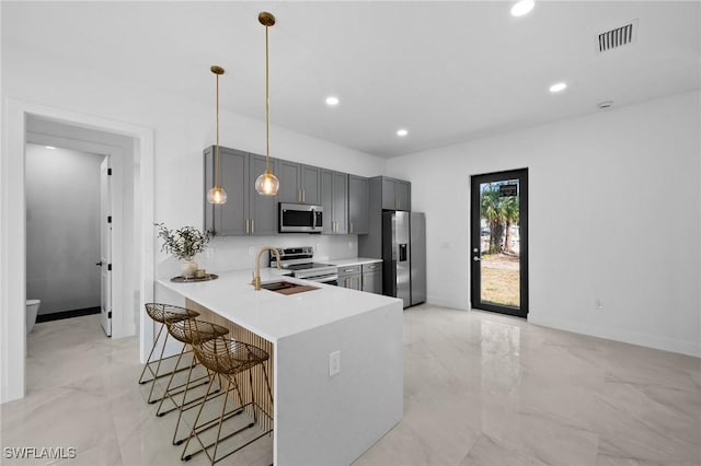 kitchen featuring marble finish floor, a breakfast bar area, gray cabinets, light countertops, and appliances with stainless steel finishes