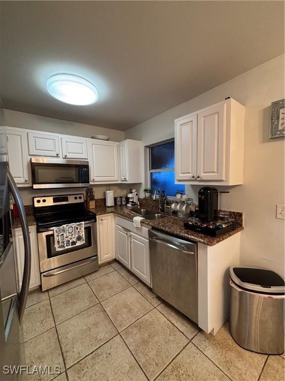 kitchen with stainless steel appliances, dark stone counters, white cabinetry, and a sink