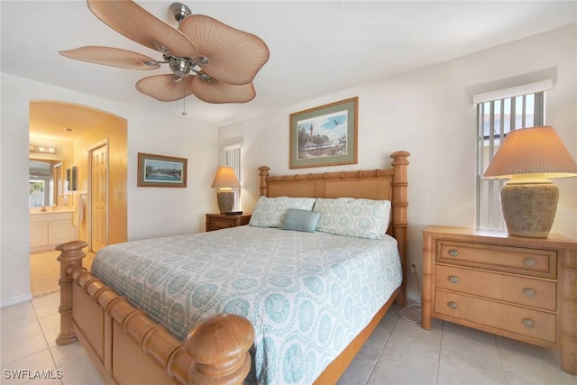 bedroom with light tile patterned floors, baseboards, arched walkways, a ceiling fan, and ensuite bathroom