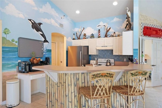 kitchen featuring under cabinet range hood, a peninsula, high end refrigerator, tasteful backsplash, and white range with electric cooktop