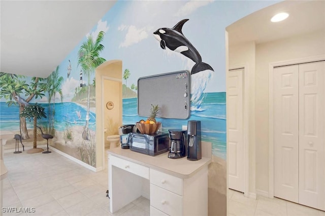 kitchen featuring wallpapered walls, baseboards, arched walkways, light countertops, and white cabinetry