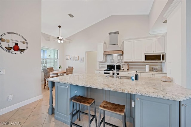 kitchen with appliances with stainless steel finishes, a breakfast bar area, custom exhaust hood, white cabinetry, and a sink