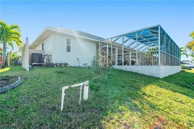 rear view of house featuring a lanai, central air condition unit, a lawn, and stucco siding