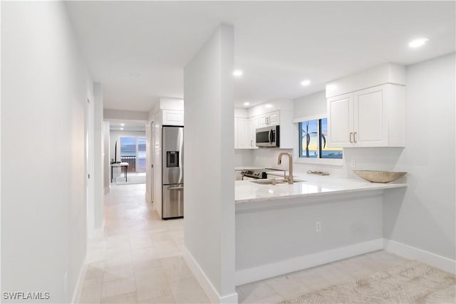 kitchen with baseboards, stainless steel appliances, a sink, and white cabinets