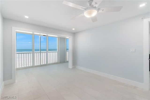 unfurnished room featuring ceiling fan, a water view, and baseboards