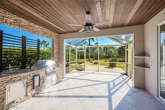 view of patio / terrace with ceiling fan, glass enclosure, an outdoor kitchen, a sink, and grilling area