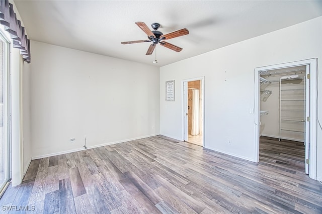 unfurnished bedroom with a walk in closet, ceiling fan, baseboards, and wood finished floors