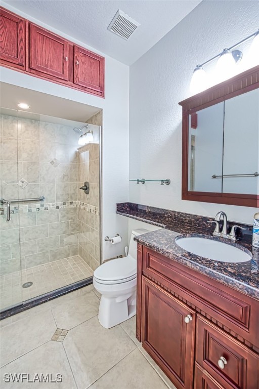 bathroom featuring tile patterned flooring, toilet, vanity, visible vents, and a stall shower