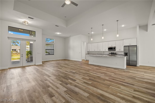 unfurnished living room with light wood-style flooring, a high ceiling, visible vents, and baseboards