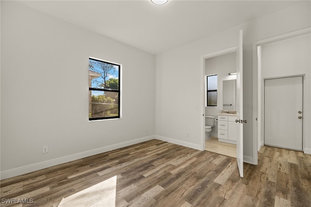 unfurnished bedroom with light wood-style floors, baseboards, and ensuite bathroom