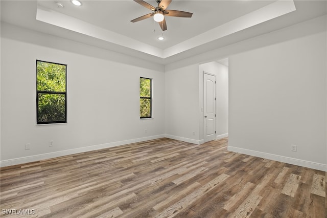 empty room with wood finished floors, recessed lighting, a raised ceiling, and baseboards