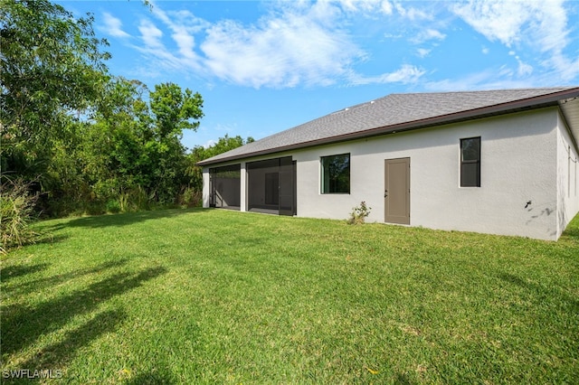 rear view of house featuring a shingled roof, a sunroom, a yard, and stucco siding